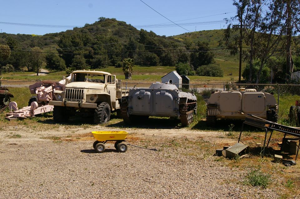 tan military truck, gray tracked vehicle, and tan tracked vehicle parked outside with a yellow wagon in front