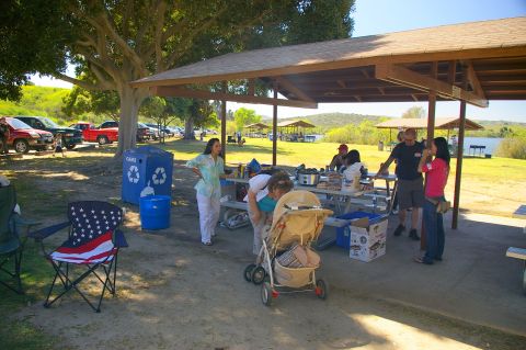 1986 Ford Bronco - A group enjoys a sunny day picnic under a covered pavilion near a lake, with several vehicles parked nearby.