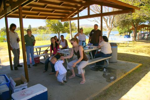 1986 Ford Bronco - A group of people enjoy a picnic under a covered shelter by a lake on a sunny day.