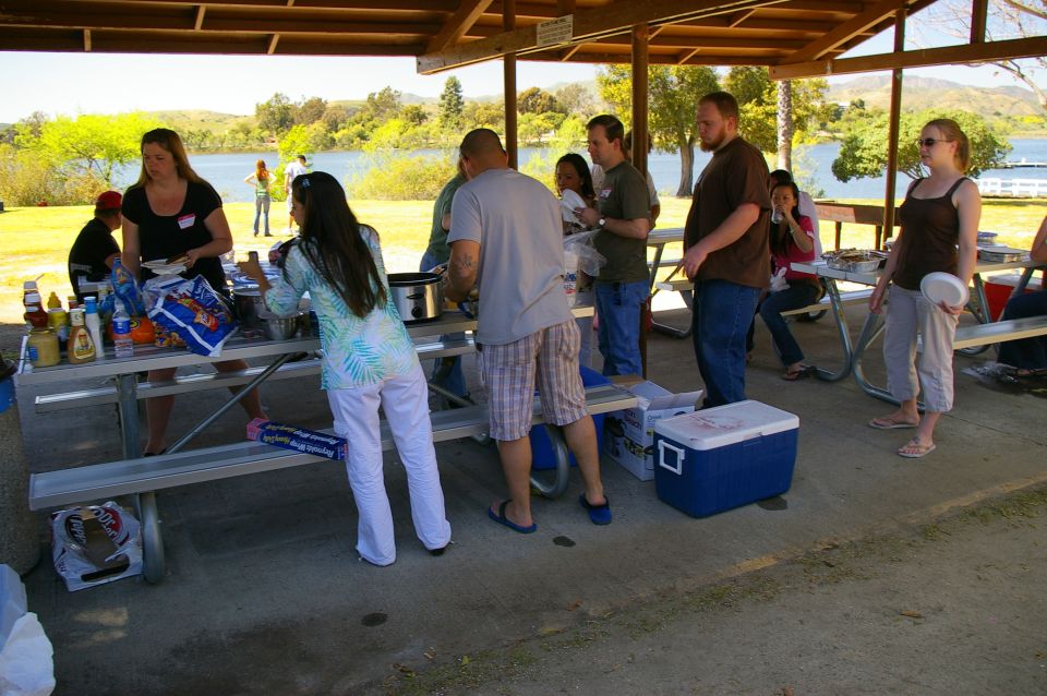 People gathered around a picnic table under a shelter, with a lake in the background