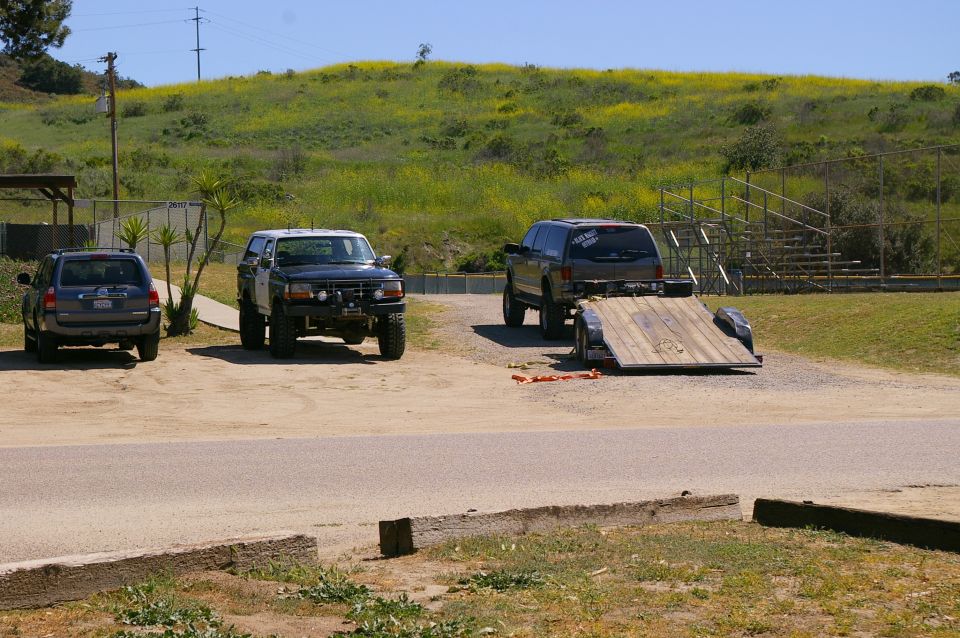 Three SUVs parked in a lot with a trailer attached to one; grassy hill in background