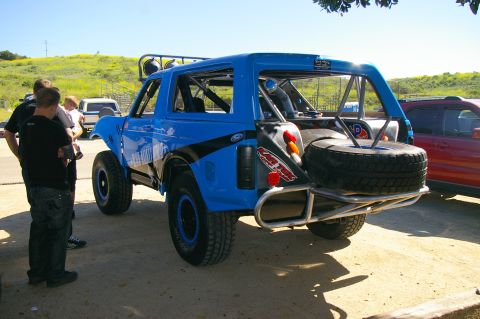1986 Ford Bronco - Modified 1986 Ford Bronco with roll cage and spare tire, parked outdoors with other vehicles.
