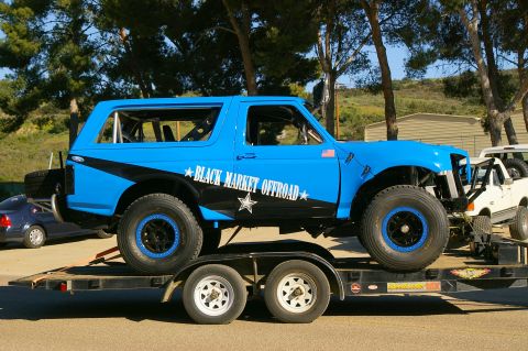 1986 Ford Bronco - Modified 1986 Ford Bronco on a trailer, with 'BLACK MARKET OFFROAD' graphics. Another truck is visible.