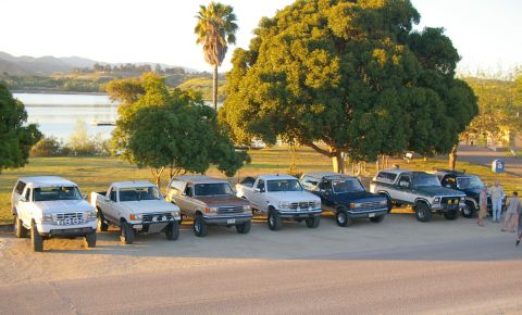 1986 Ford Bronco - A collection of Ford trucks and Broncos are parked side-by-side in a scenic outdoor location.