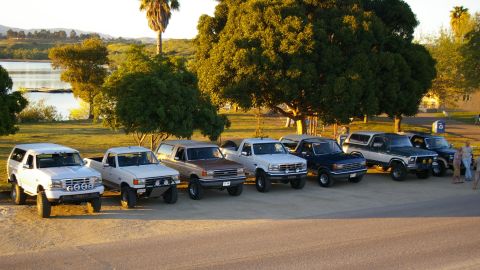 1986 Ford Bronco - A row of Ford trucks and SUVs, including a white 1992 Bronco, are parked outdoors near a body of water.