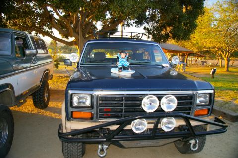 1986 Ford Bronco - A dark blue Ford Bronco with a tan lower body and a brush guard is parked next to another vehicle.