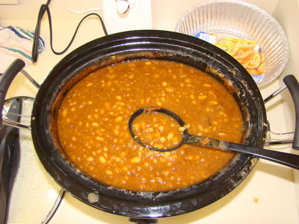Slow cooker filled with baked beans and a ladle