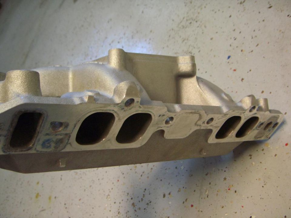 Bare aluminum V8 intake manifold on bench showing rectangular port face and bolt holes