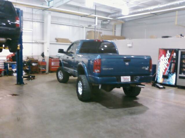 Blue 2006 Dodge 2500 pickup truck with lifted suspension and chrome wheels, seen from the rear in a garage