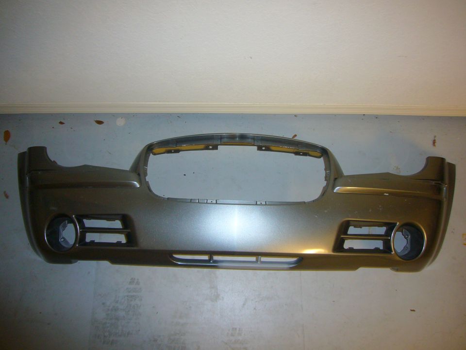 Bronze metallic front bumper cover removed from a car, leaning against a wall