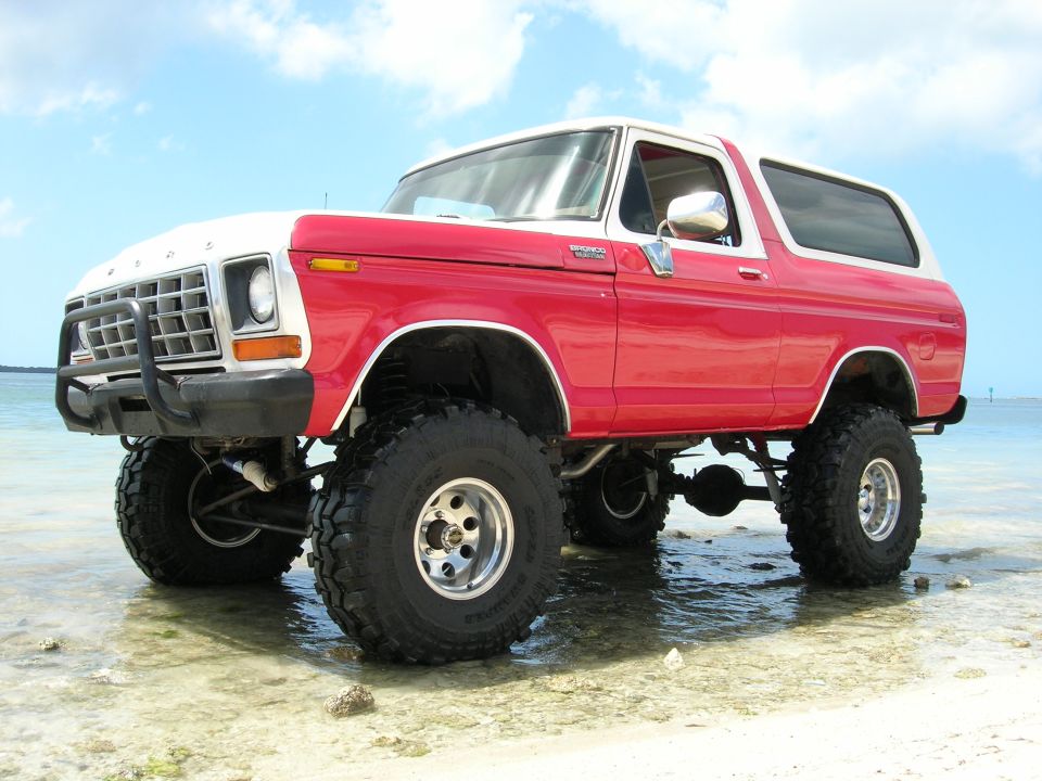 Red and white lifted 1978 Ford Bronco parked in shallow water