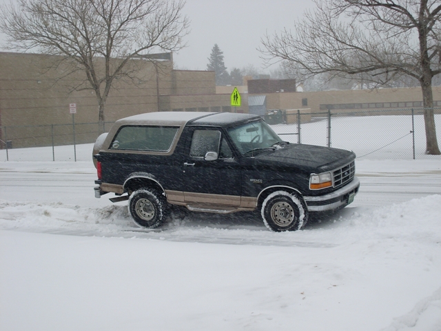 Black and tan Ford Bronco in snow, 3/4 front view. Snow is falling