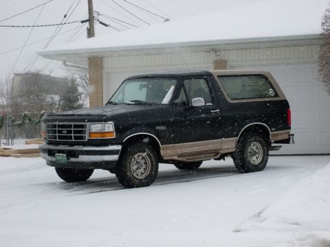 1996 Ford Bronco - A black and tan 1996 Ford Bronco is parked in front of a garage during a snowfall.