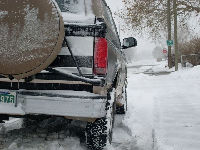 Rear view of tan SUV with spare tire in snow, showing license plate 975