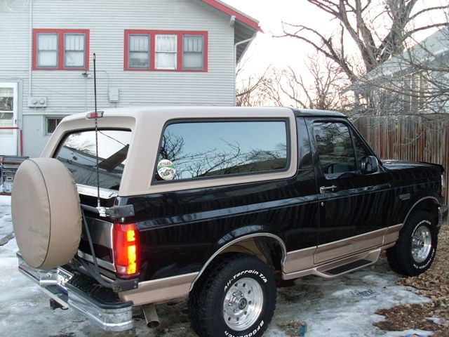 Black and tan Ford Bronco parked in front of a house. Spare tire mounted on the back