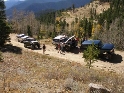 1996 Ford Bronco - A group of off-road vehicles navigate a mountain trail, with one vehicle stopped for attention.