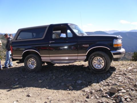 1996 Ford Bronco - A black 1996 Ford Bronco is parked on a rocky overlook with mountains in the background.