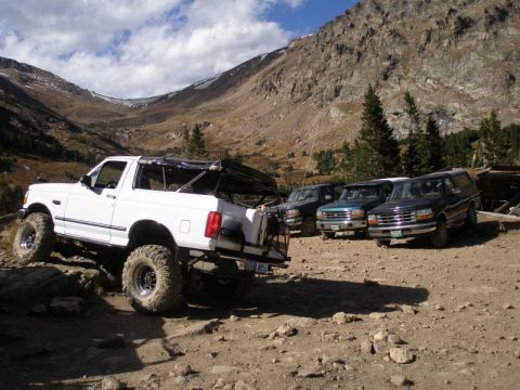 1996 Ford Bronco - A lifted white 1996 Ford Bronco navigates a mountain trail, with several other SUVs parked in the background.