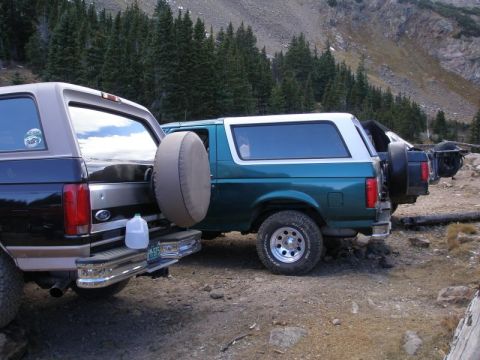1996 Ford Bronco - Several Ford Broncos are parked on a dirt road in a mountainous, wooded area.