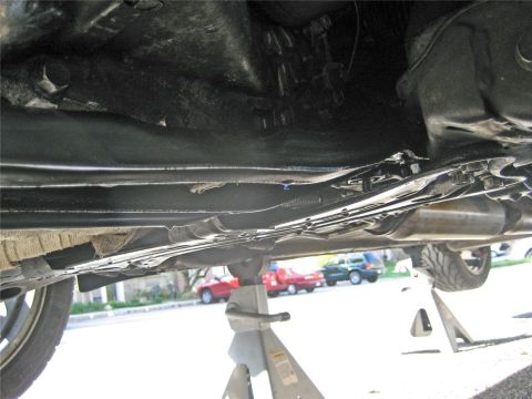 1993 Ford Probe - The underside of a vehicle is shown, supported by jack stands, with other vehicles parked on the street behind it.
