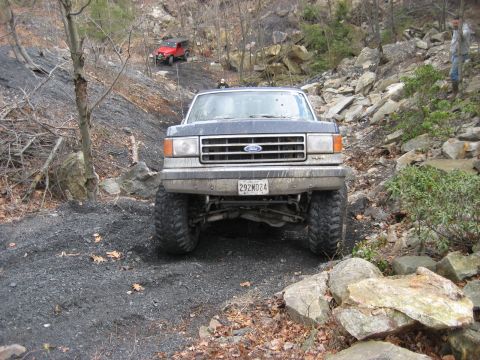 1991 Ford Bronco - Ford Bronco tackles a challenging off-road course, with a red SUV following.