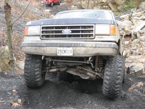 1991 Ford Bronco - This Ford truck is navigating a rough, rocky terrain with large off-road tires.