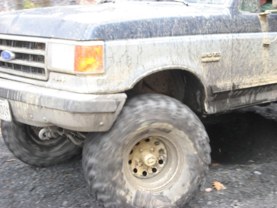 Mud-covered Ford truck front corner with large tires