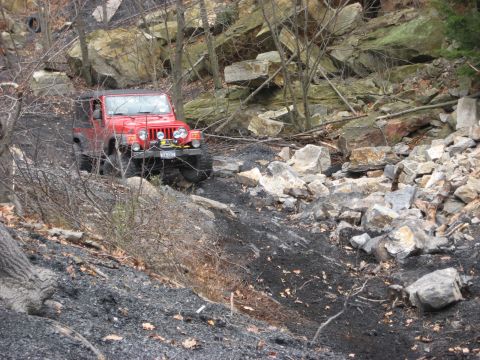 1991 Ford Bronco - A red Jeep Wrangler tackles a challenging off-road course with steep, rocky inclines.