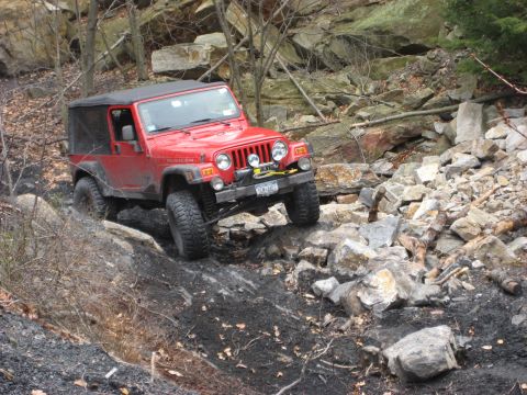 1991 Ford Bronco - Jeep Wrangler Rubicon TJ model tackling challenging off-road terrain on a rocky slope.