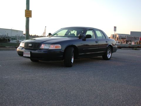 1999 Ford Crown Victoria - This Ford Crown Victoria is parked in a lot near some buildings and a body of water.