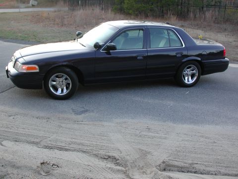1999 Ford Crown Victoria - A dark blue sedan with chrome wheels is parked on a paved surface, showing its side profile and interior.