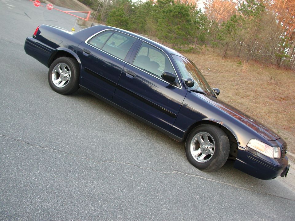 Dark blue sedan parked on an asphalt road, angled from the front-right. Chrome wheels and black trim are visible