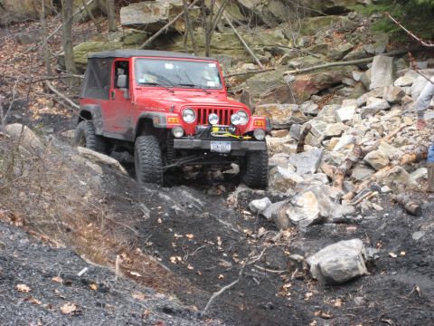 1991 Ford Bronco - A red Jeep Wrangler Rubicon tackles a challenging rocky terrain during an off-road event.