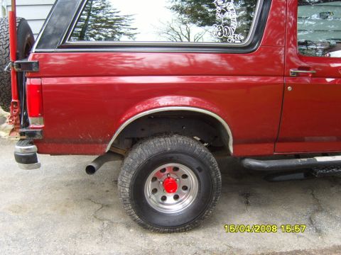 1989 Ford Bronco - Rear view of a red SUV showing its spare tire and a decorative sticker on the rear window.