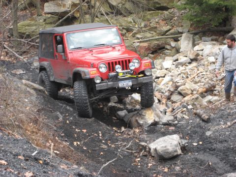 1991 Ford Bronco - A red Jeep Wrangler tackles a challenging rocky path during an off-road event.