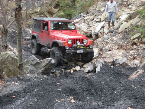 1991 Ford Bronco - A red Jeep Wrangler navigates a rocky, off-road trail with a person observing from higher ground.