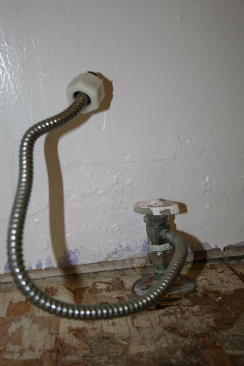 2003 Jeep TJ - Plumbing supply lines and shut-off valves are visible against a white wall, with damaged flooring below.