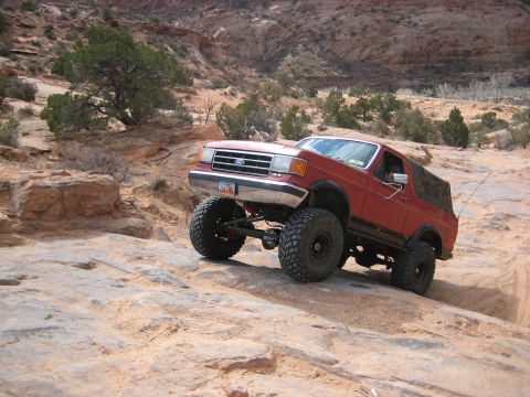 1990 Ford Bronco - This lifted Ford Bronco navigates a challenging rocky trail in a desert landscape.
