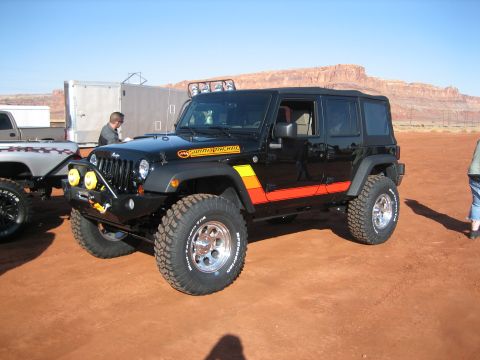 1990 Ford Bronco - A black Jeep Wrangler is parked on a dirt surface with a trailer and another truck nearby.