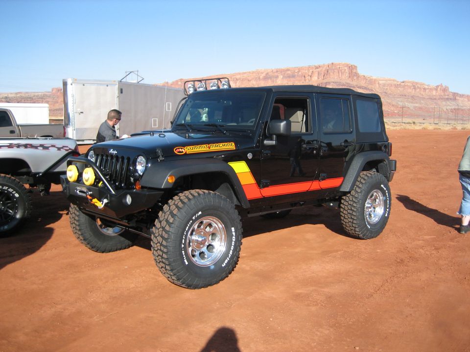 Black Jeep Wrangler with orange and yellow stripes, aftermarket bumper, and roof lights