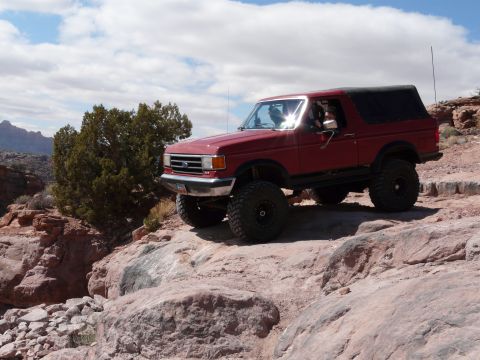 1990 Ford Bronco - This red 1990 Ford Bronco navigates a , rocky landscape, likely during an off-road event.