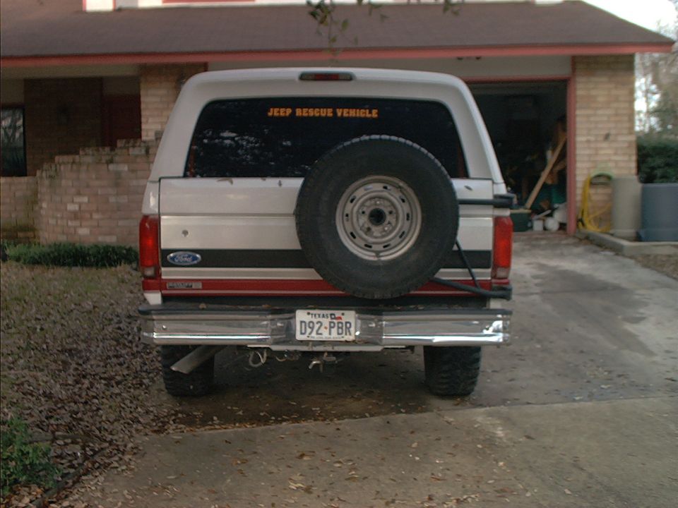 Rear of white Ford Bronco with spare tire carrier and 'Jeep Rescue Vehicle' window decal in a driveway