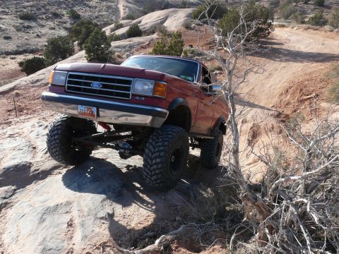 1990 Ford Bronco - This modified Ford Bronco is tackling a challenging off-road trail in a desert landscape.