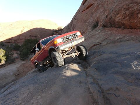 1990 Ford Bronco - A red 1990 Ford Bronco navigates a steep, rocky incline during an off-road excursion.