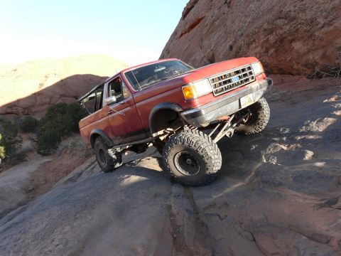 1990 Ford Bronco - This modified Ford Bronco navigates a steep, rocky trail under a clear blue sky.