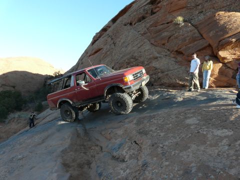 1990 Ford Bronco - A red 1987 Ford Bronco navigates a steep, rocky trail under a clear blue sky.
