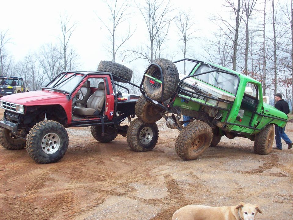 Red and green doorless caged 4x4 buggies parked tail-to-tail in a muddy gravel lot