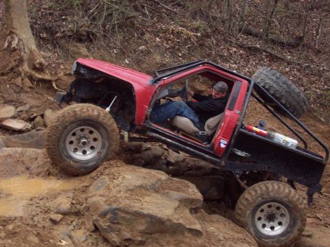 1978 Ford Bronco - A red off-road vehicle navigates a challenging rocky and muddy terrain.