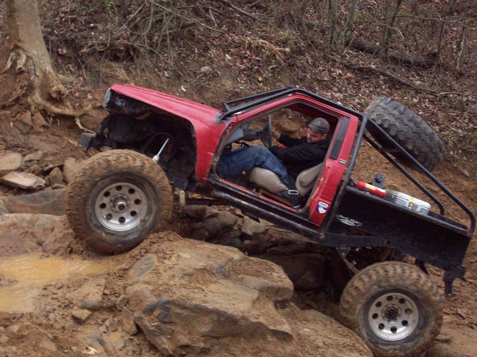 Red off-road vehicle with large tires climbing over rocks and mud