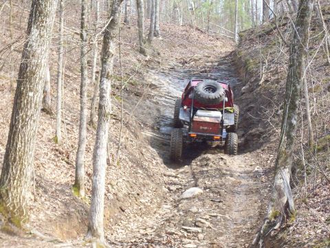 1978 Ford Bronco - A red off-road vehicle navigates a challenging, rocky incline through a dense forest.